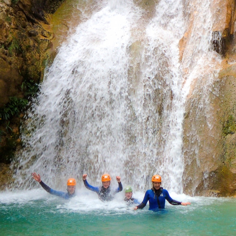 Grupo de personas debajo de una cascada de 7 metros con las manos levantadas en la actividad de barranquismo en Sierra de Guara