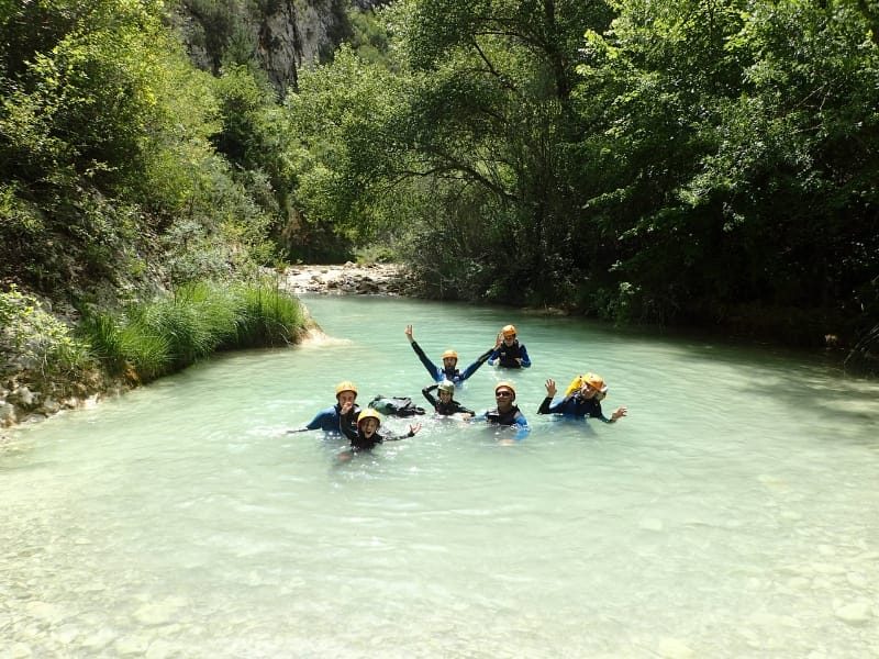 familia en el agua azul turquesa de un barranco de Sierra de Guara mirando a cámara practicando barranquismo familiar en Huesca