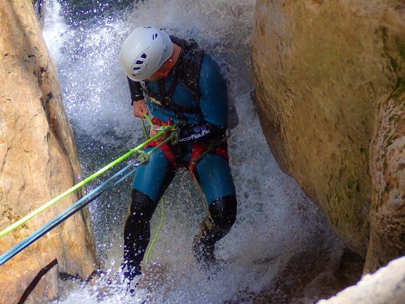 Hombre haciendo barranquismo en Guara con una cuerda de rapel descendiendo junto a una cascada