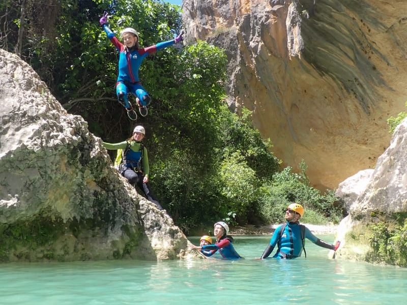 niña tirandose al agua turquesa de un barranco en la actividad barranquismo en familia Huesca