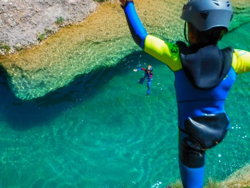 niño tirándose al agua turquesa de un barranco mientras el otro le mira durante la actividad barranquismo en familia Huesca