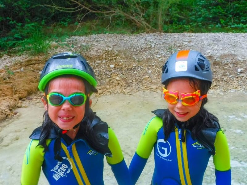 dos niñas con cascos y gafas de buceo en la orilla de un barranco en la actividad barranquismo en familia Huesca